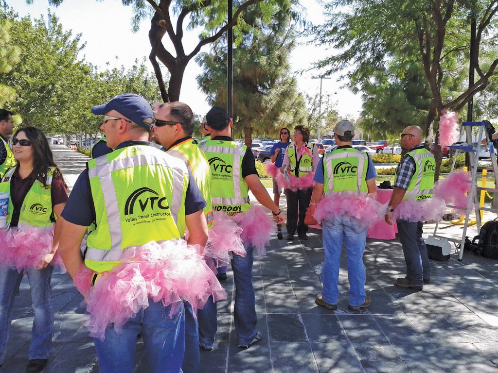 Pink tutus complement project safety vests as employees gather for the Mesa Arts Center’s Pink Tutus event supporting breast cancer awareness month.