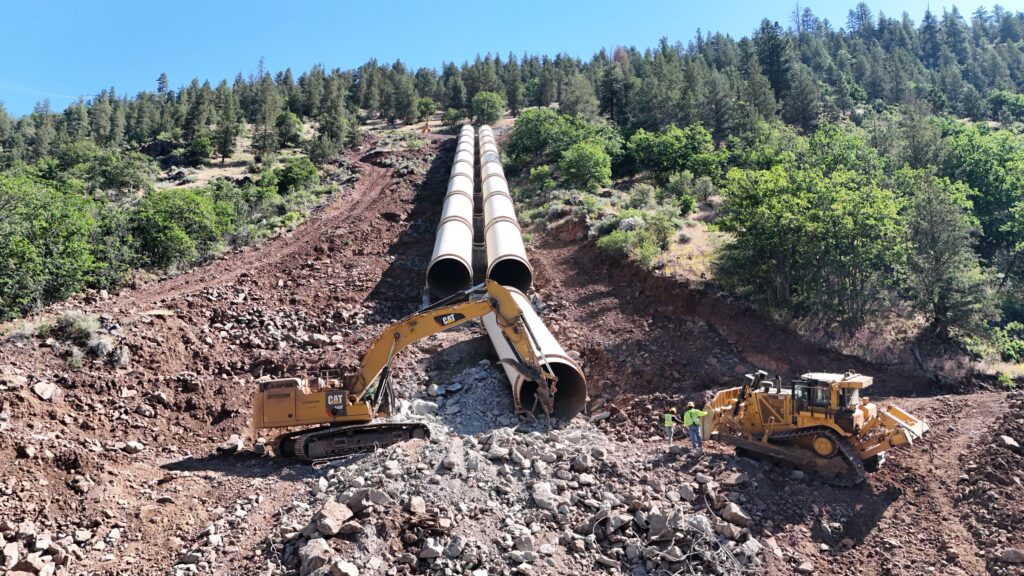 One of the most challenging aspects of demolishing the JC Boyle earthen dam in Oregon was the removal of double penstocks, each about 10 feet in diameter. Water was kept level for about two miles, then dropped down the steep mountain in penstocks to drive power. The team brought in track line excavators to repel equipment down the steep slopes.