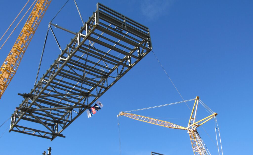 A crew lifts the final preassembled truss into place on the southeast half of the building at the Spent Fuel Handling Project at Idaho National Laboratory. Flags representing each branch of the U.S. military adorn the truss.