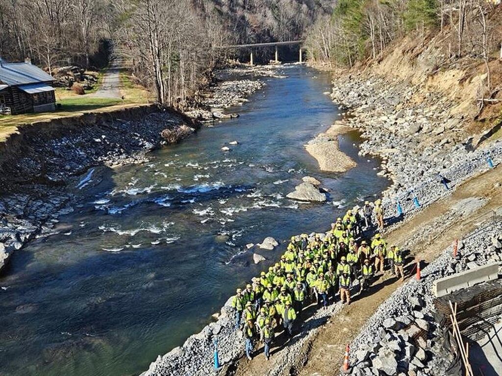 The Kiewit team gathers on the rebuilt causeway, restored after the storm washed away more than 8,000 tons of riprap. On the left, a neighboring property near the jobsite bears the scars of the flood, its riverbank deeply gouged by Helene’s wrath.