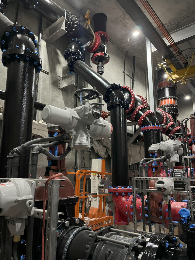 At the Ballona Creek facility, pumps draw water from the wet well and distribute it through two separate flow paths. One header routes water vertically through the roof to the ozone disinfection system, while the other directs flow to the Hyperion Water Reclamation Plant via a bypass line. 